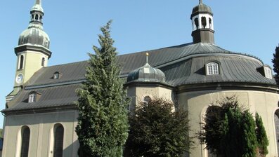 Eine barocke Kirche mit geschwungenem Dach und zwei Türmen, umgeben von grünen Bäumen