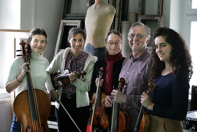 Fünf Musikerinnen und Musiker mit Streichinstrumenten posieren lächelnd in einem Atelier oder Probenraum