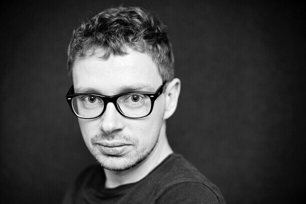 Schwarz-Weiß-Porträt von Marcin Markowicz mit Brille und kurzem, leicht gelocktem Haar, der ernst in die Kamera blickt