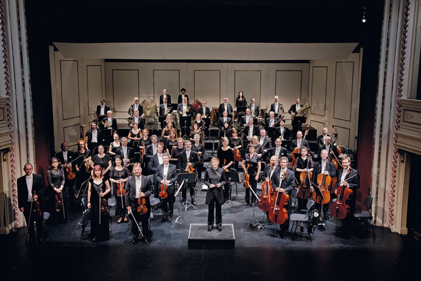 Sinfonieorchester auf einer Bühne, mit einer Dirigentin in der Mitte