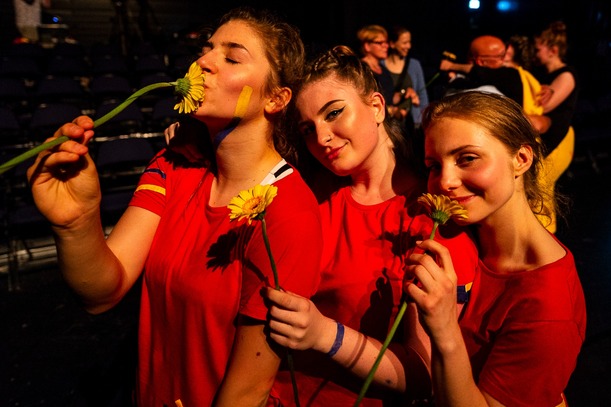 Drei junge Frauen in roten Shirts mit gelben Blumen in der Hand feiern eine Theateraufführung