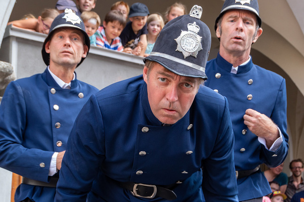 Drei Schauspieler in historischen britischen Polizeiuniformen spielen eine humorvolle Szene